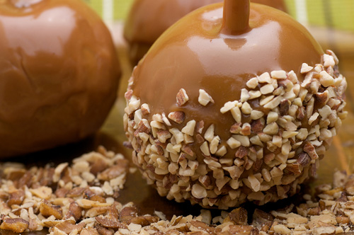 three carmel apples, one dipped in crushed nuts