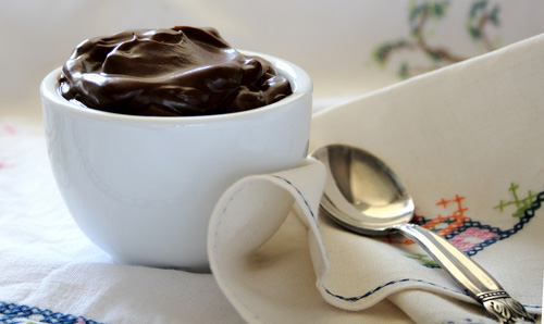 chocolate pudding in a white bowl next to a spoon and napkin