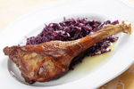 cooked goose leg next to shredded purple cabbage on a white plate