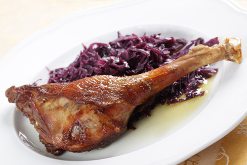 cooked goose leg next to shredded purple cabbage on a white plate