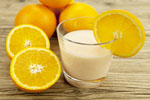 orange julius in a glass next to whole and half oranges