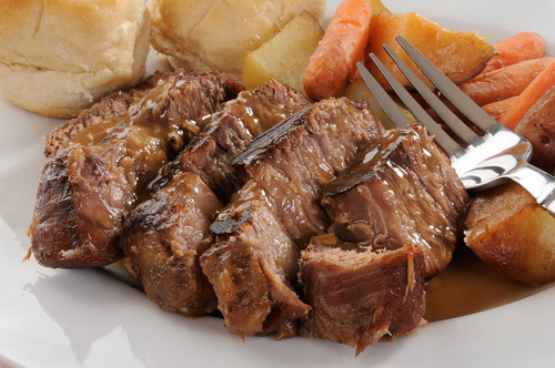 four slices of pot roast next to potatoes and carrots