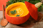 pumpkin soup inside a raw pumpkin next to a wooden spoon