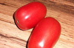 two raw oval shaped roma tomatoes on a board